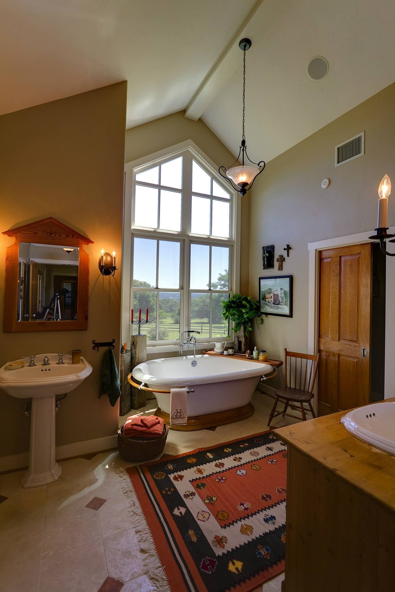 Bathroom with a tall window overlooking a landscape, a freestanding tub, and a decorative rug.