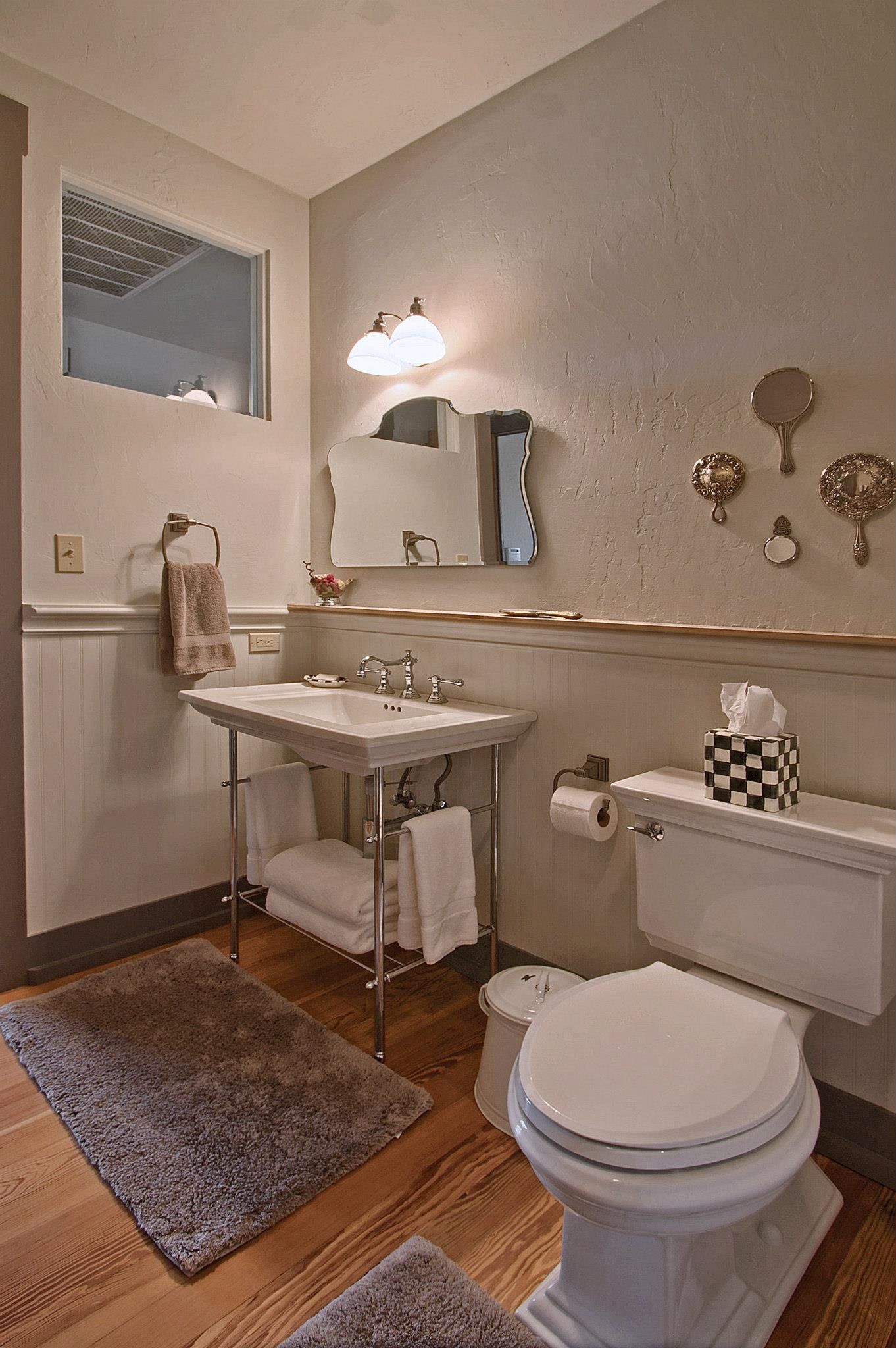 Bathroom with a pedestal sink, toilet, and decorative wall mirrors; neutral tones, wood floors.