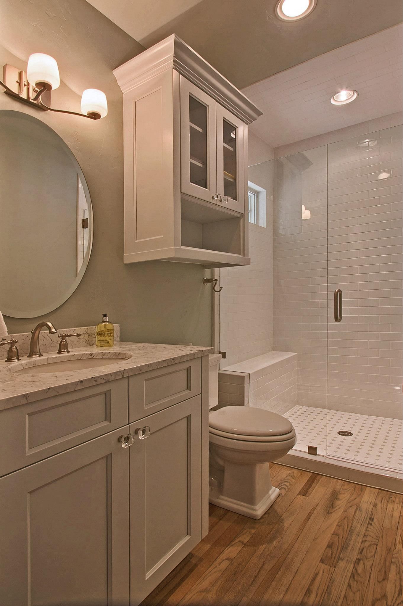 Bathroom with a white vanity, a round mirror, and a glass shower with wood-look flooring.