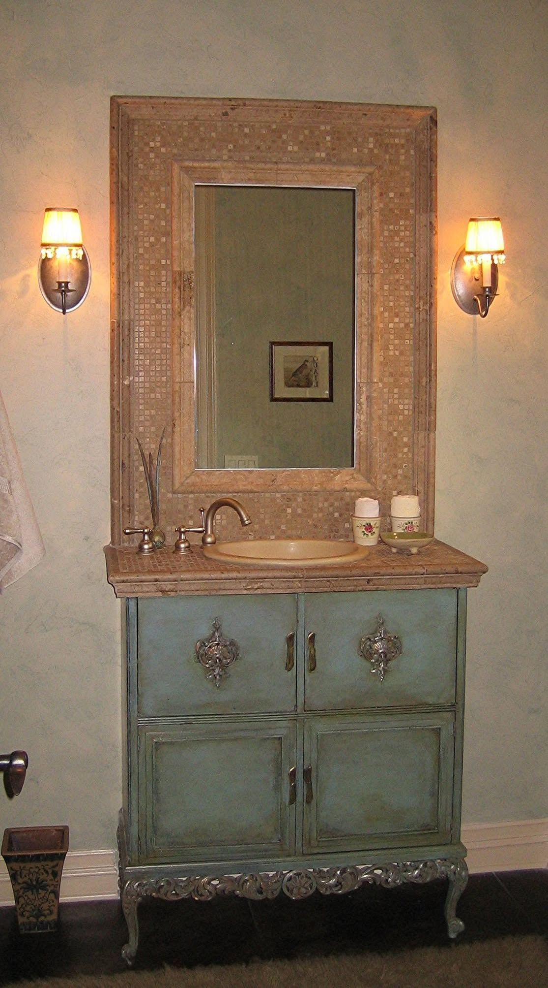 Bathroom vanity with blue cabinet, ornate gold mirror frame, and sconces.