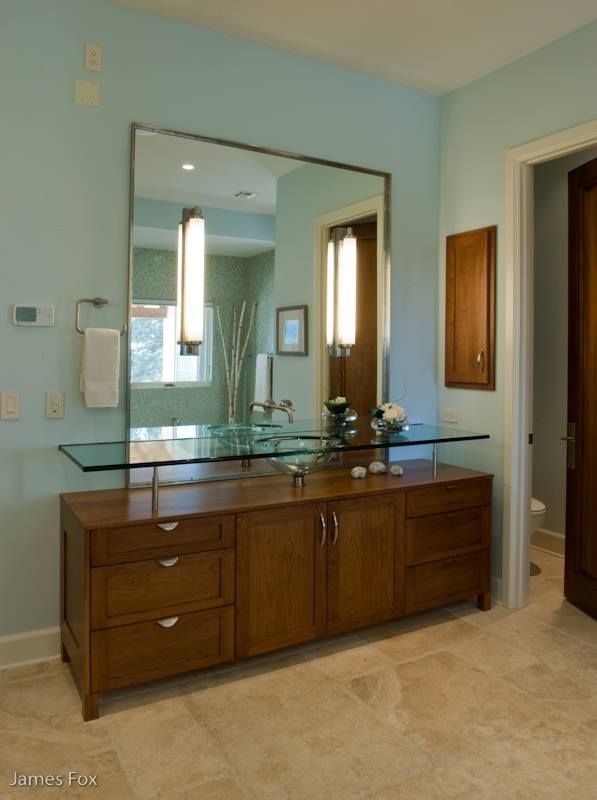 Wooden vanity with glass top and large mirror in a light blue bathroom.