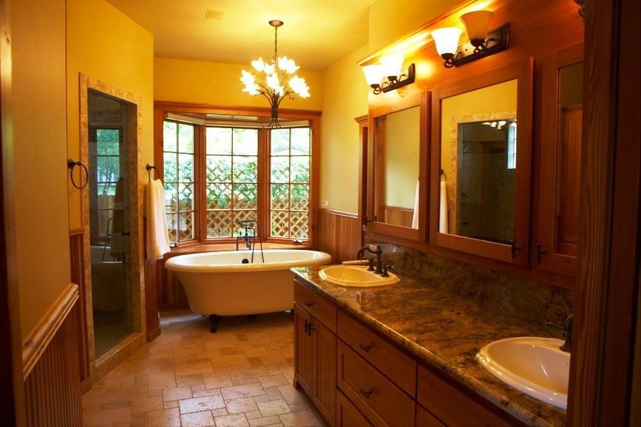 Bathroom with clawfoot tub, double vanity, and large window. Warm tones, wood accents, and chandelier.