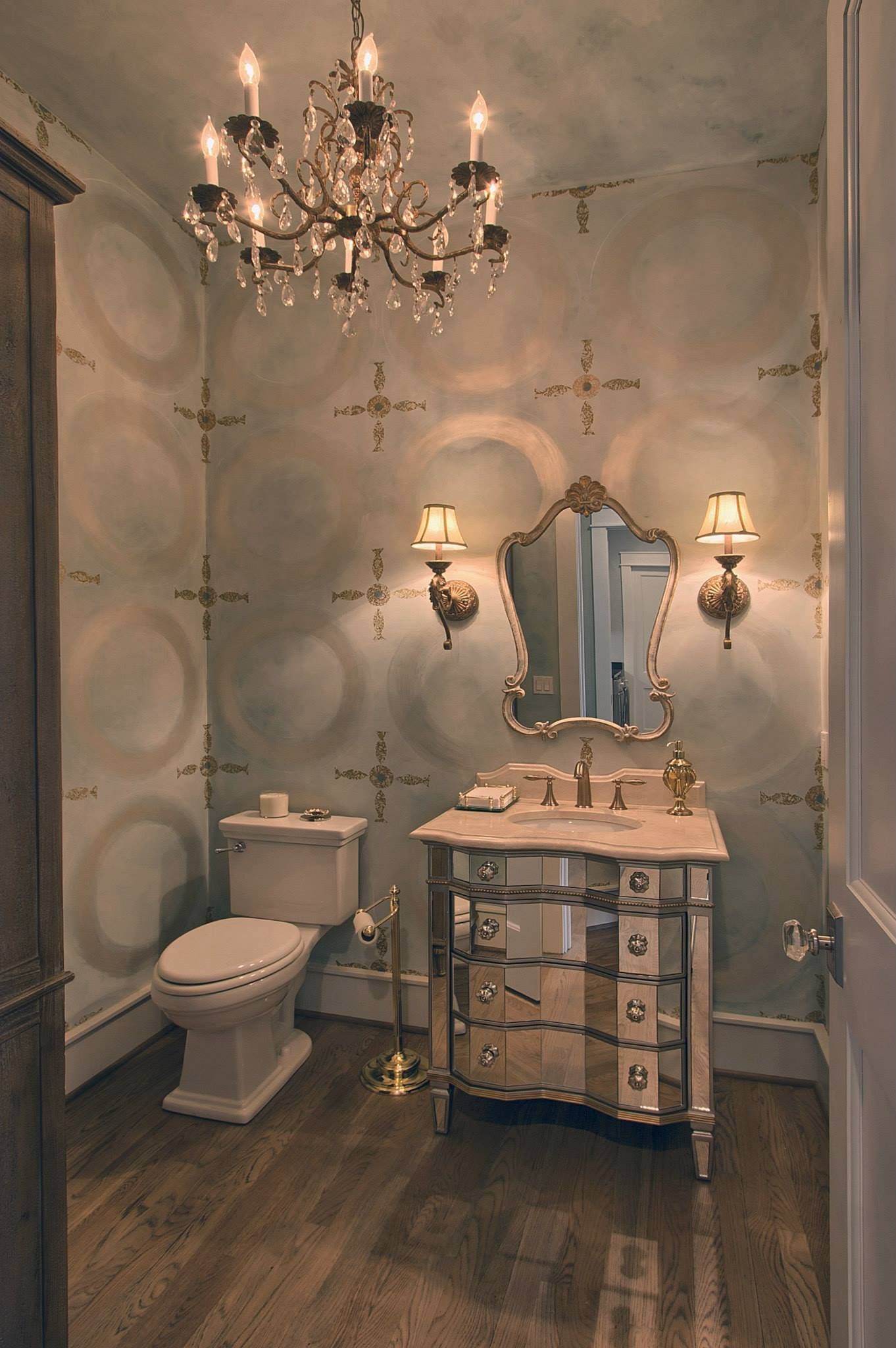 Elegant powder room with a chandelier, mirrored vanity, and patterned wallpaper.