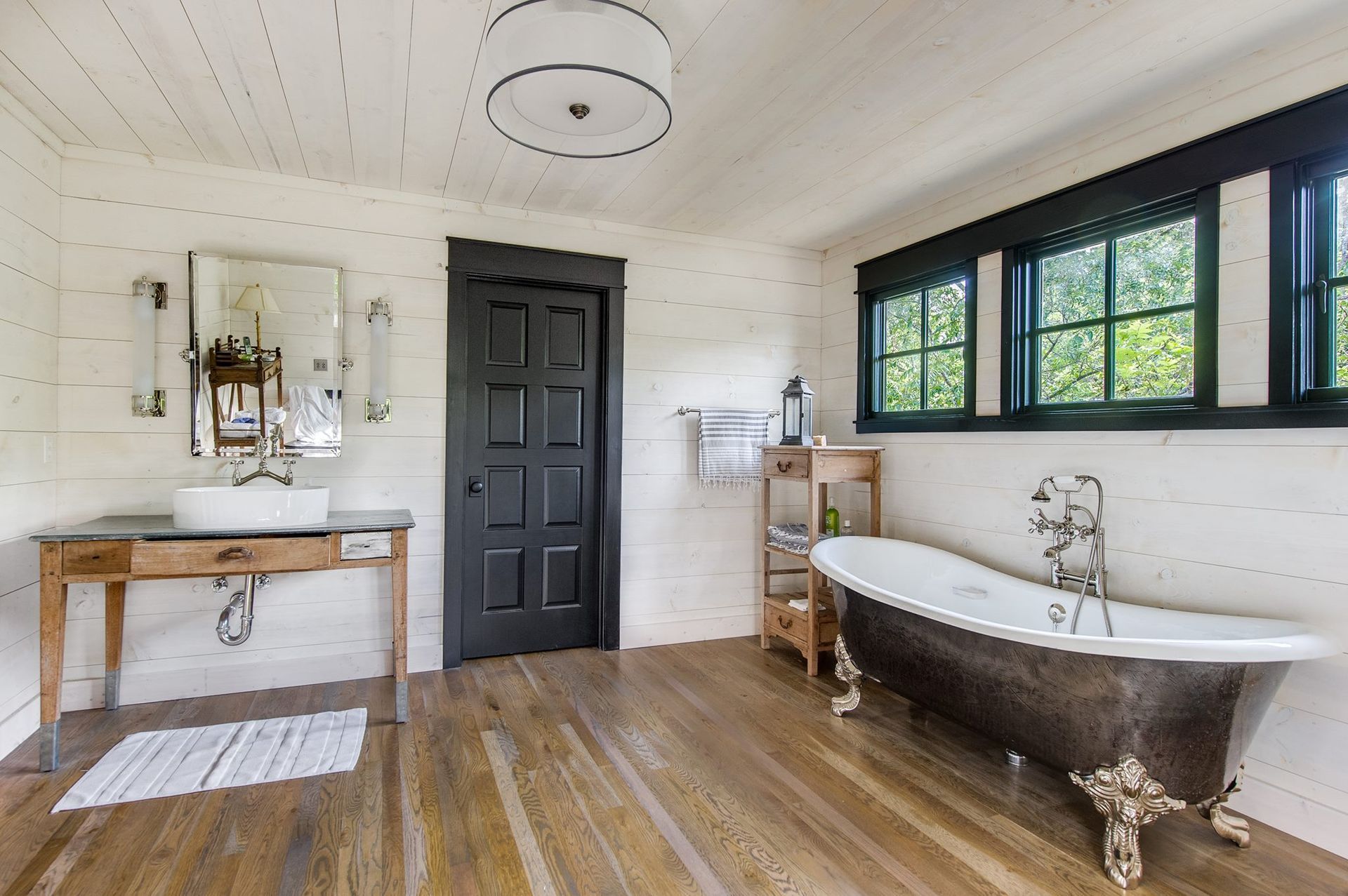 Rustic bathroom with clawfoot tub, wood floors, black trim, and white walls.