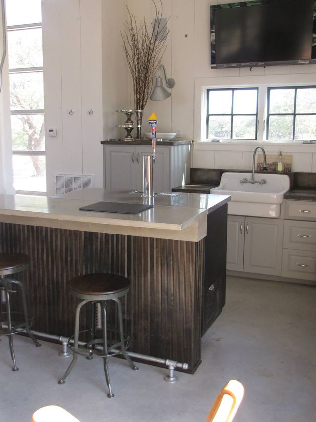 Bar with metal stools, dark wood paneling, tap, and white sink against a windowed wall.