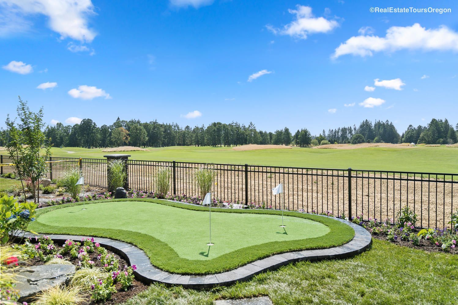There is a putting green in the backyard with a fence in the background.