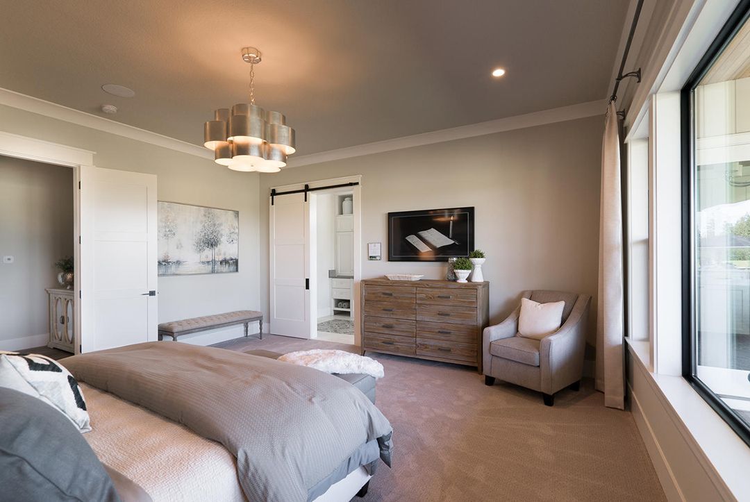 A bedroom with a bed , chair , dresser and window.