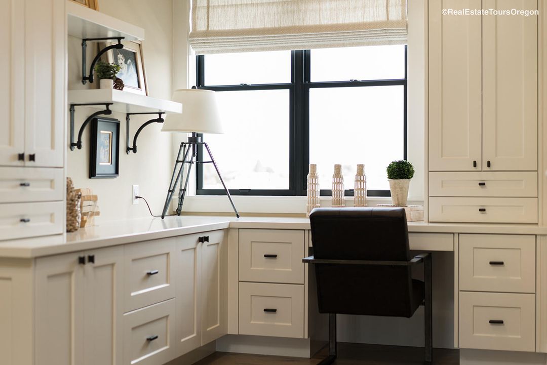 A home office with white cabinets and a black chair in front of a window.