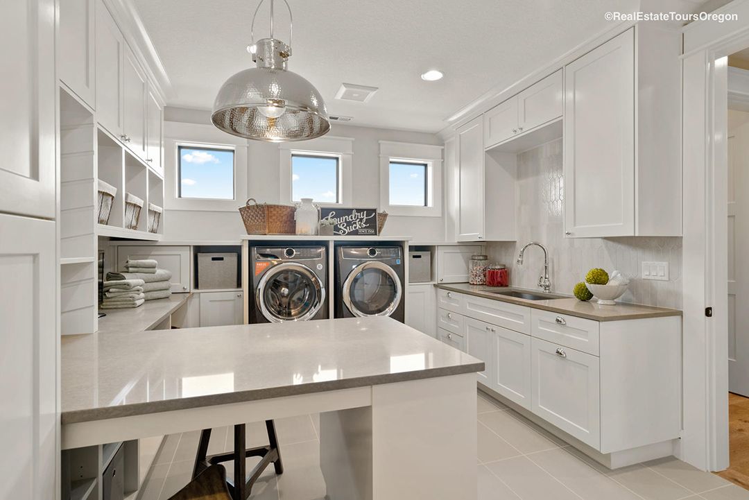A laundry room with white cabinets , a washer and dryer , a sink , and a table.