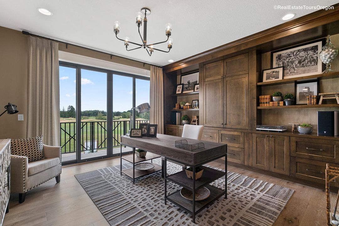 A home office with a desk , chair , shelves and a chandelier.