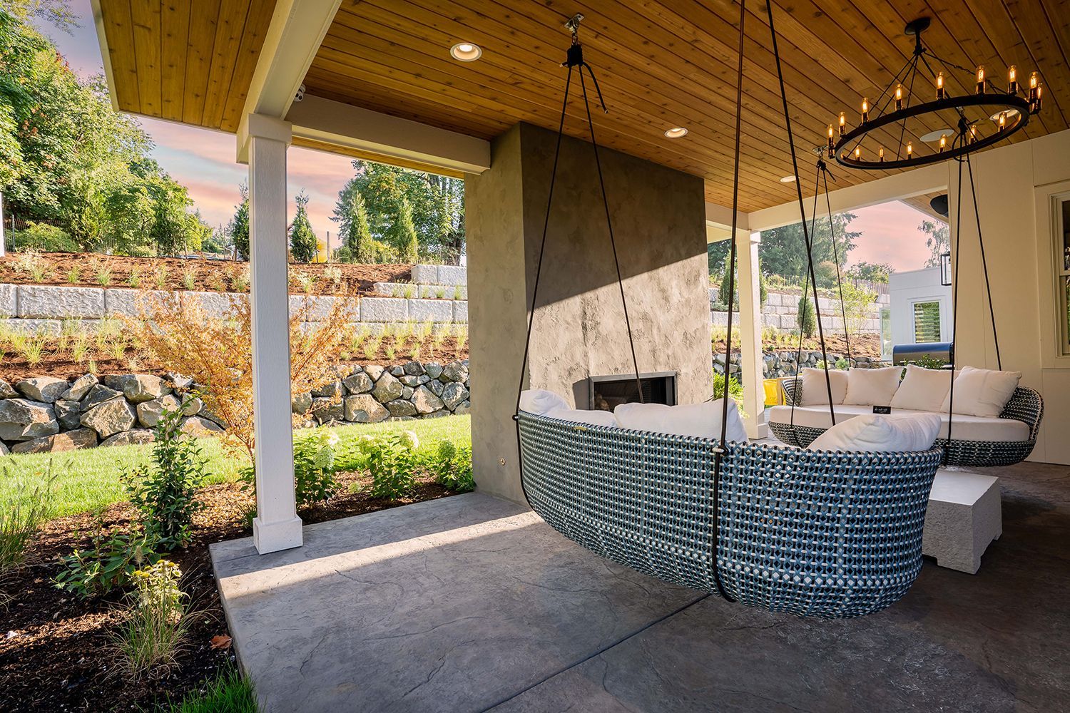 A patio with a couch hanging from the ceiling and a fireplace.