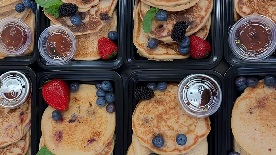 Overhead view of several containers of pancakes with berries and syrup.