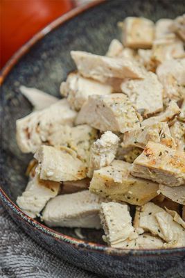 Close-up of diced cooked chicken in a dark blue bowl; pieces show herbs and seasoning.
