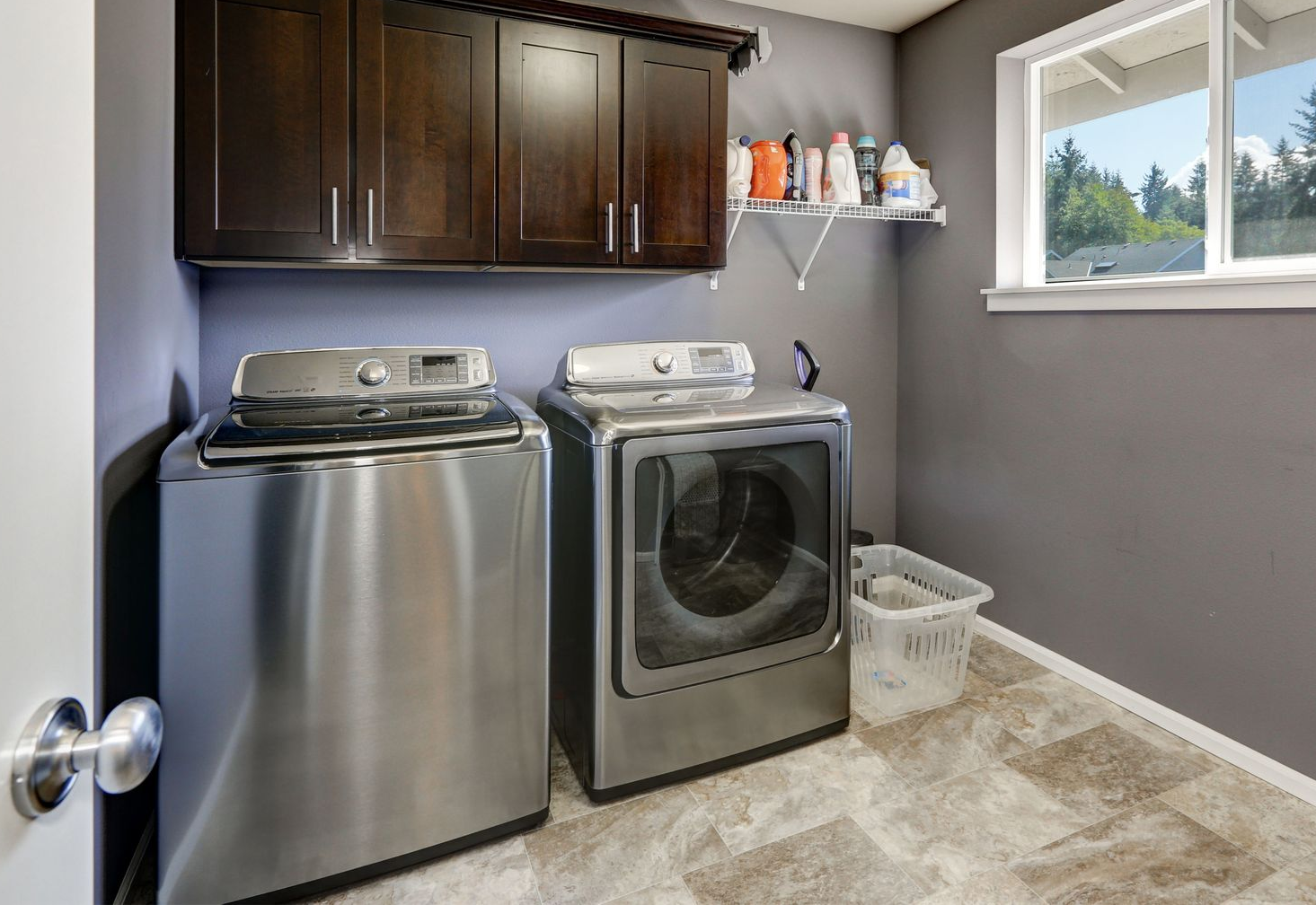 Laundry room with a washing machine, dryer, and cabinets. Gray walls, stainless steel appliances, and a window.