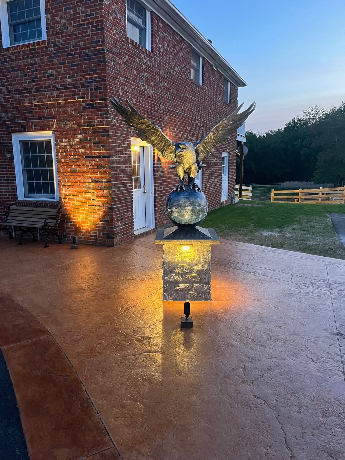 Bronze eagle sculpture atop illuminated pedestal, in front of brick building with golden spotlights.