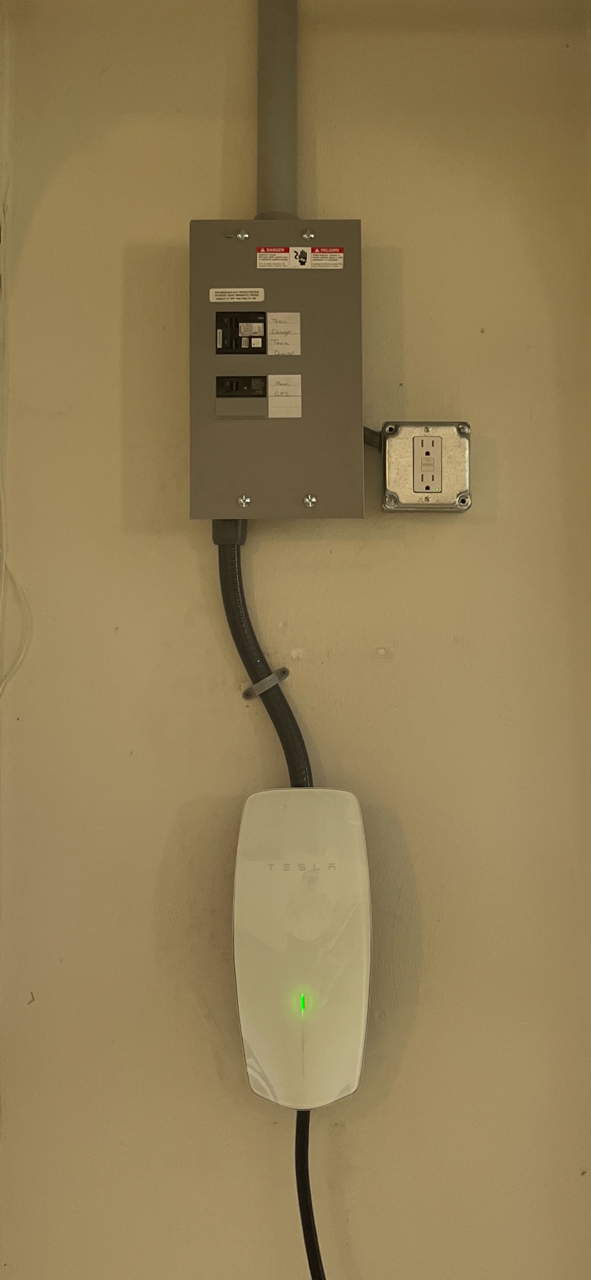 An electric vehicle charging station mounted on a beige wall, with a green indicator light.