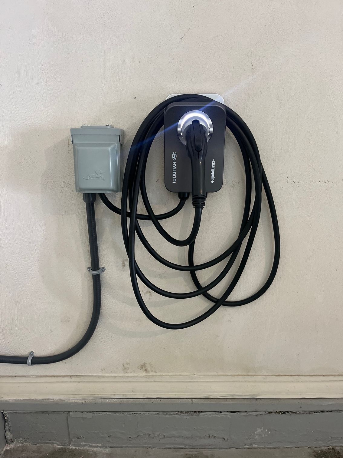 An EV charger and electrical box mounted on a white wall.