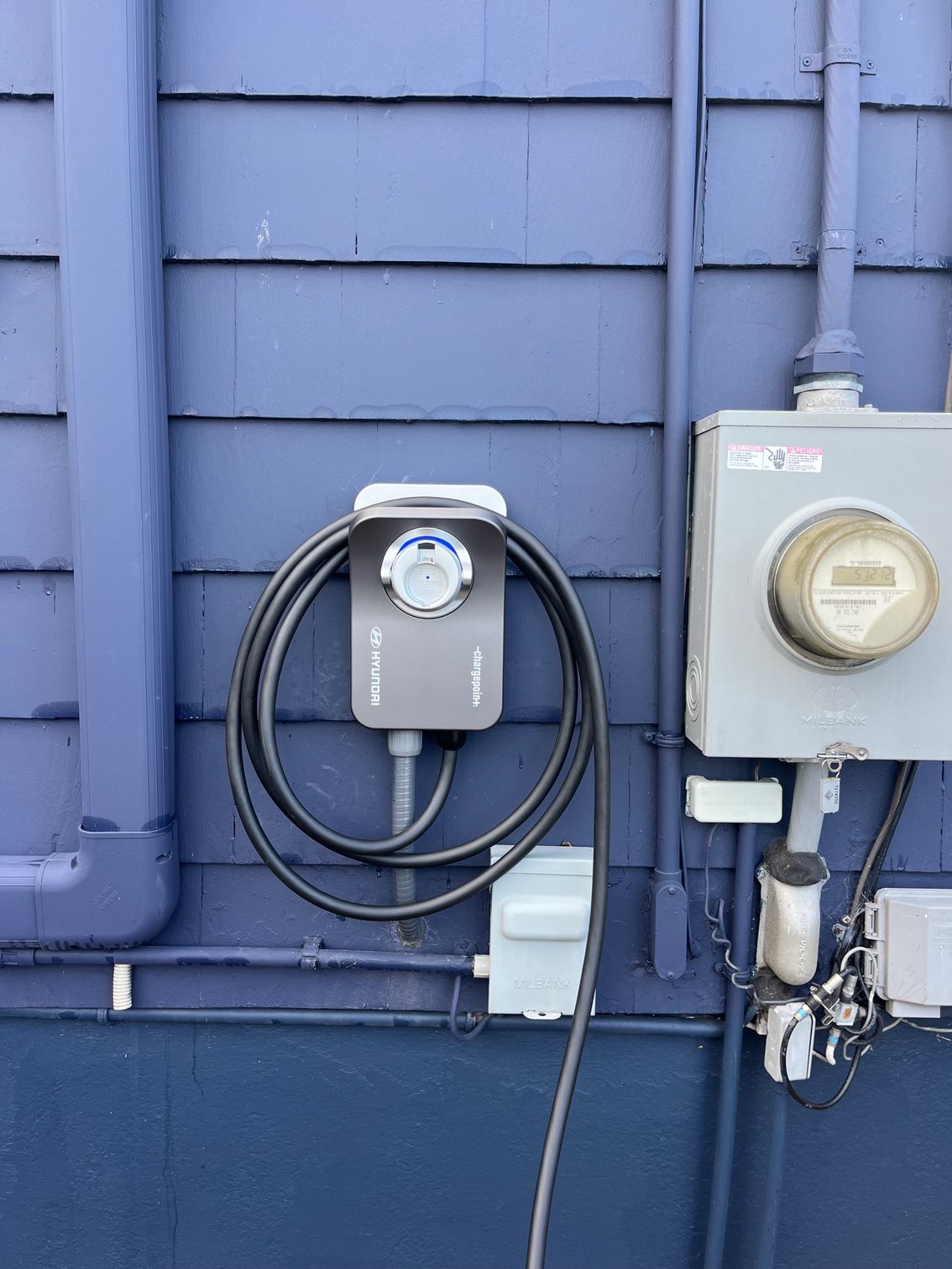 Blue wall with an EV charger, power meter, and conduit.