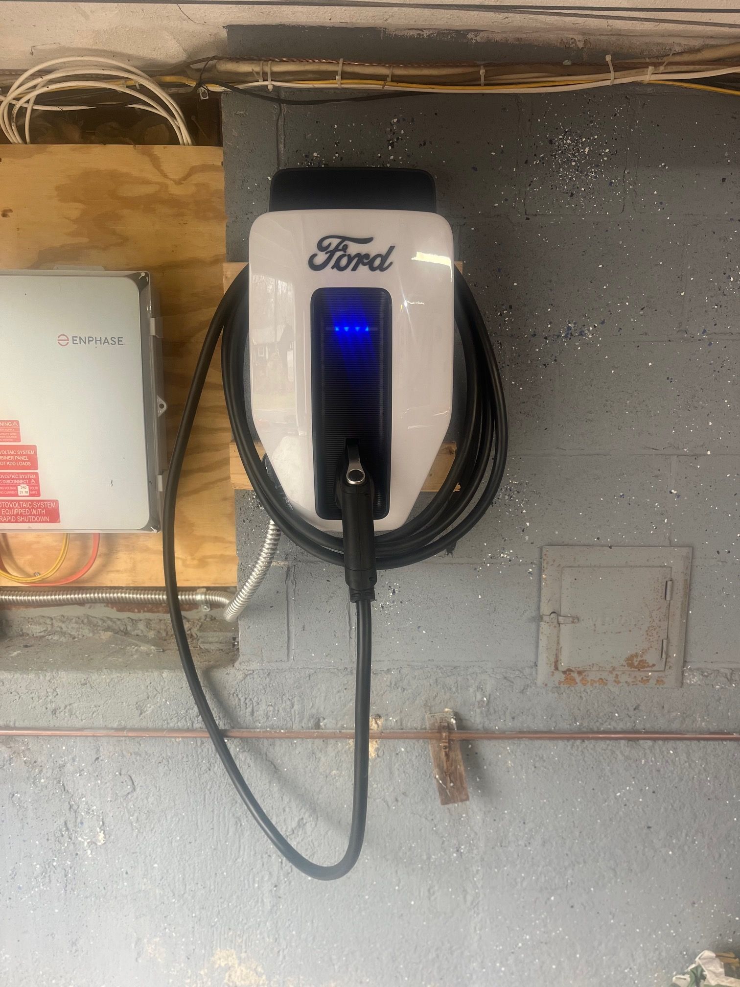 Ford EV charger mounted on a gray wall, with a charging cable attached and the blue light on.