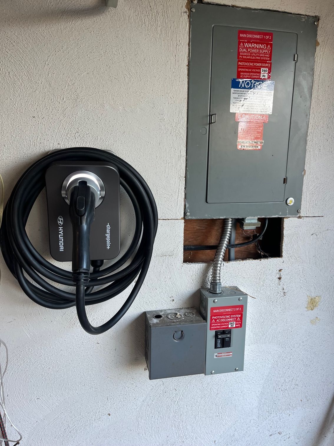 Electric vehicle charger next to a gray electrical panel and circuit breaker in a garage.