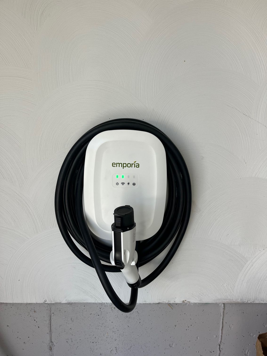 White EV charger on a wall with its black cable coiled around it.