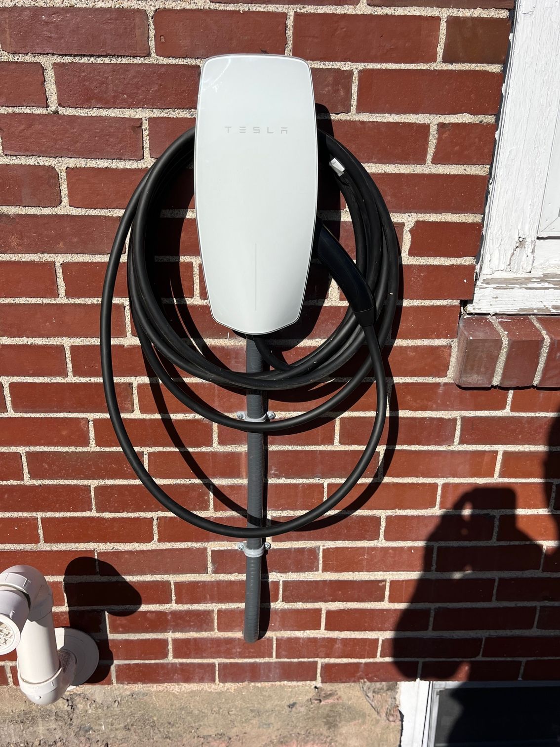 White Tesla charger mounted on a brick wall, with a coiled black cable.