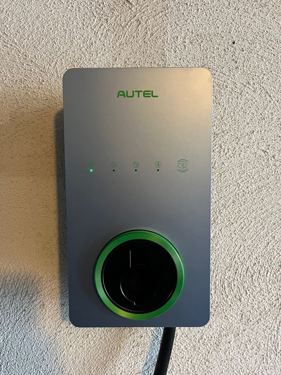 Autel EV charger, grey with green accents. A green light indicates it is on, mounted on a wall.