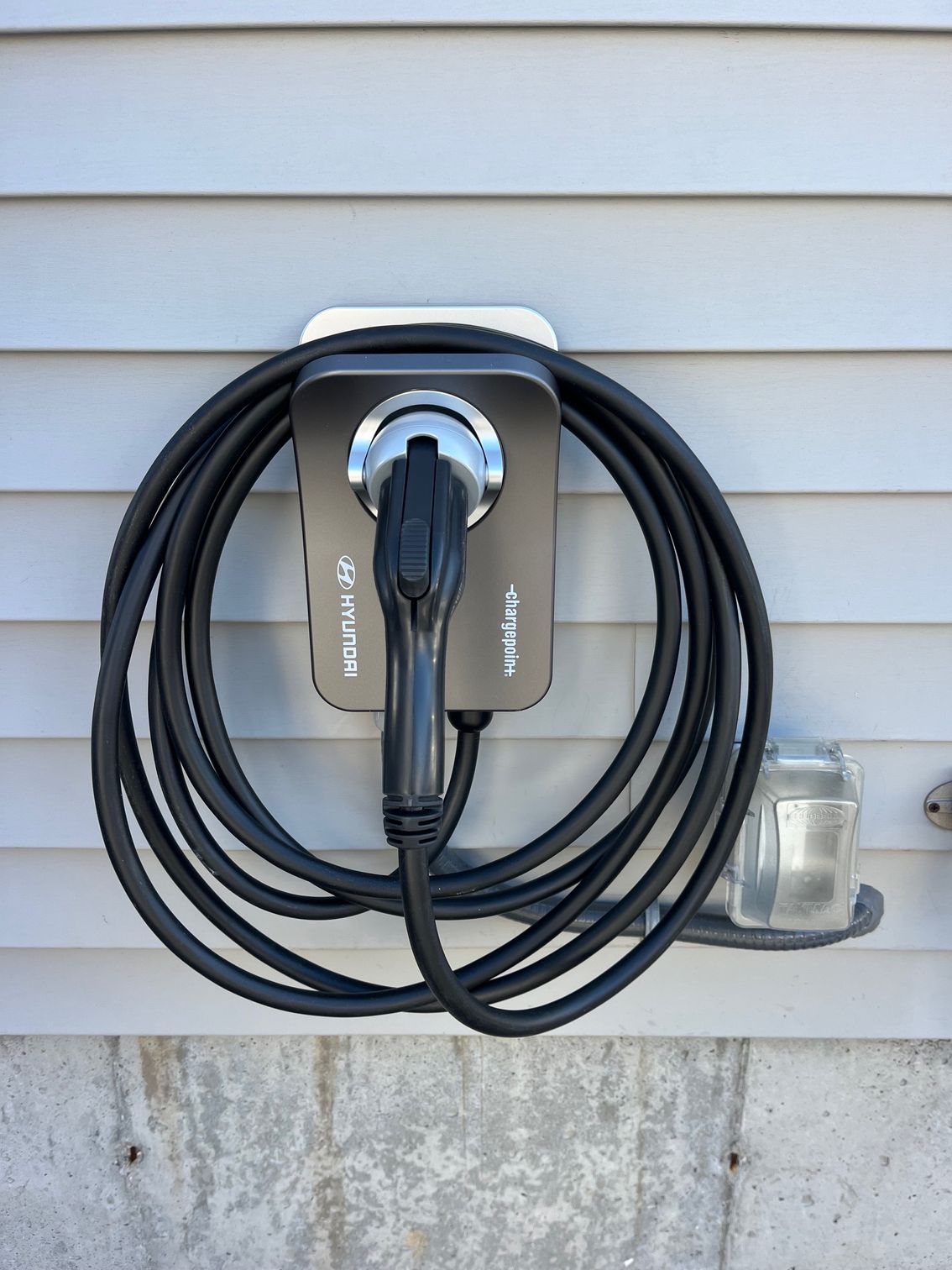 An EV charger mounted on a gray wall with a coiled black cable.