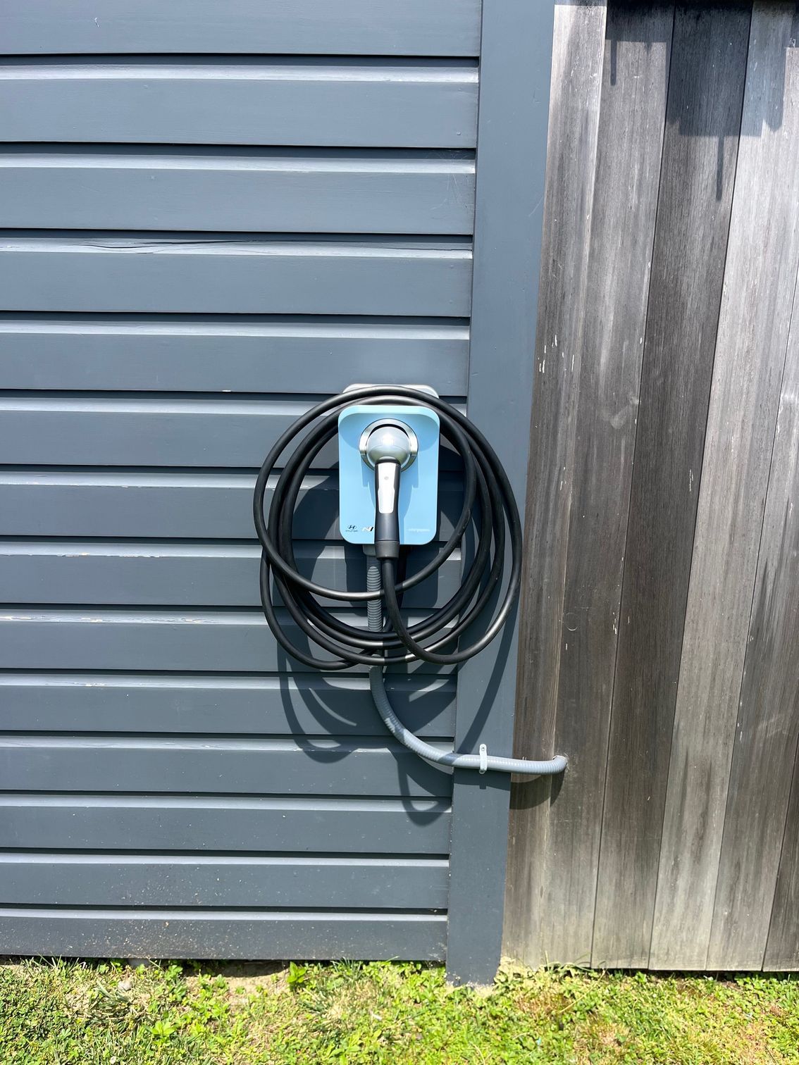 Electric vehicle charger mounted on a blue box on a gray wooden wall.