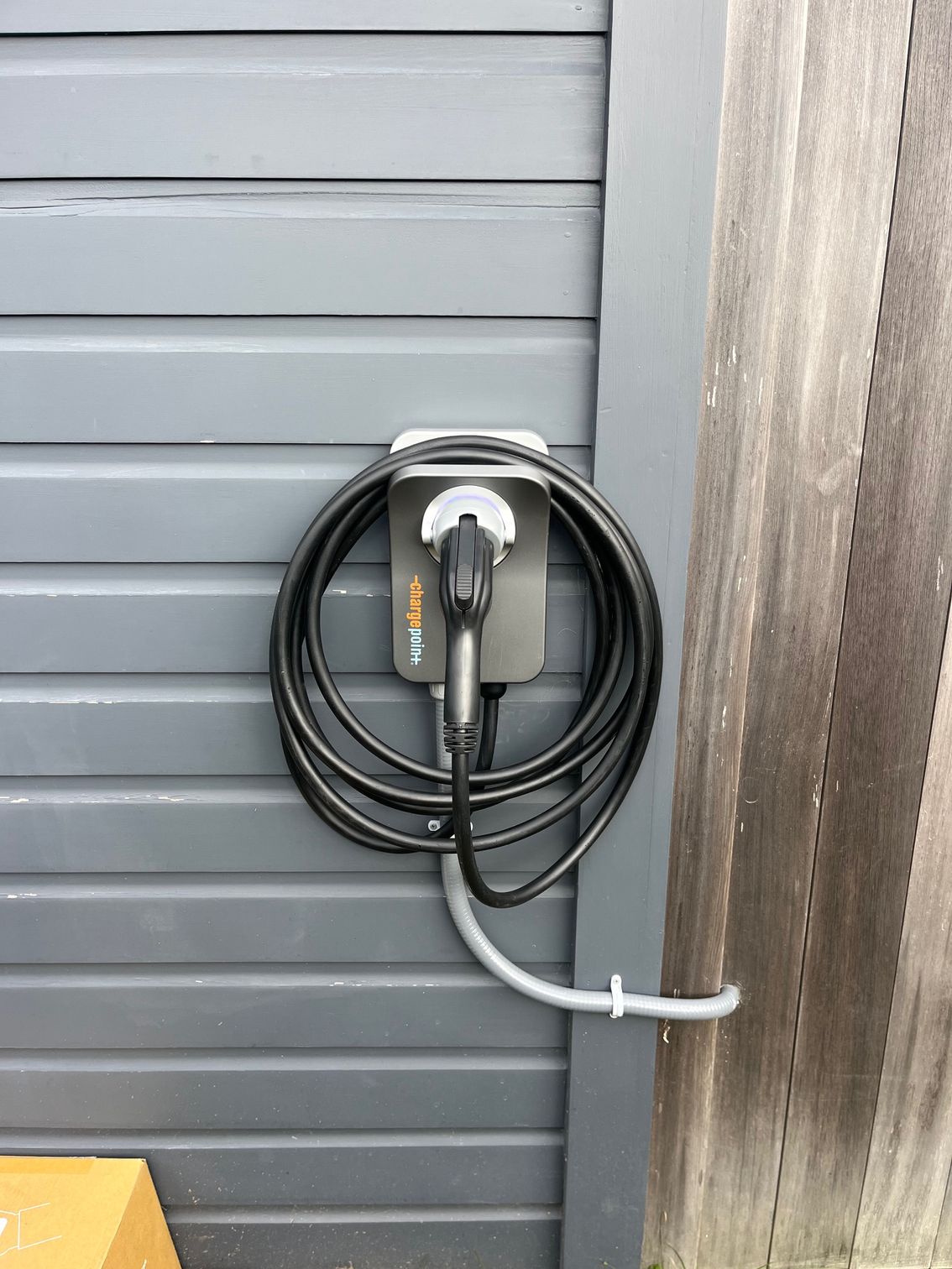 Electric vehicle charger mounted on a gray wall, cable coiled, ready for use.