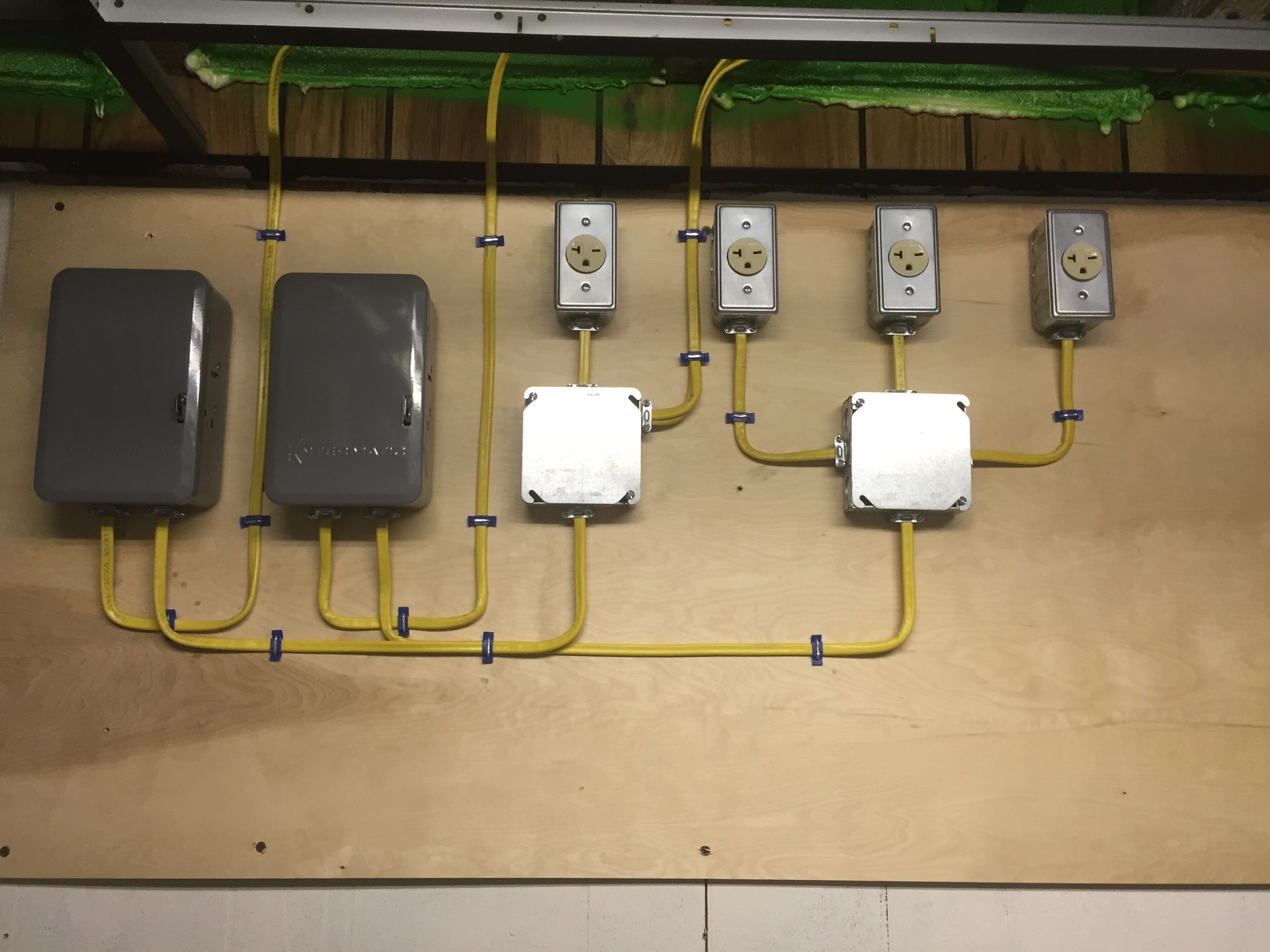 Electrical boxes and outlets on a wooden wall, connected by yellow conduit.