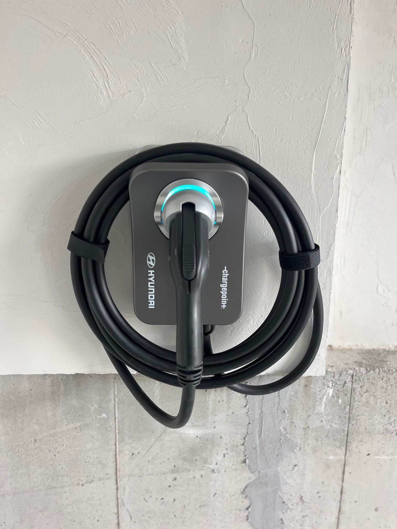 EV charger mounted on a concrete wall, with a coiled black cable and charging connector.