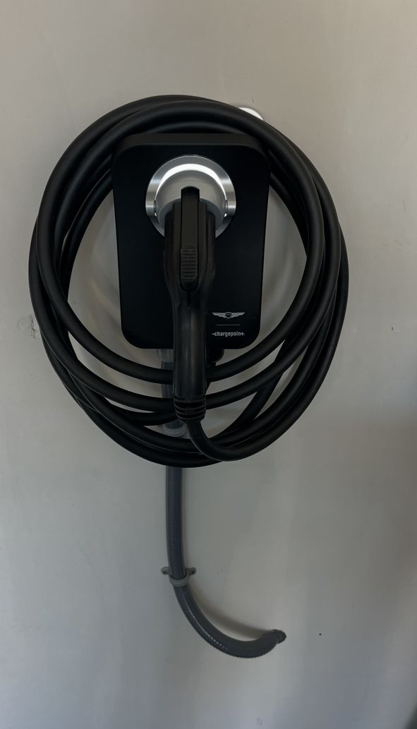 Black EV charger mounted on a white wall with coiled cable.