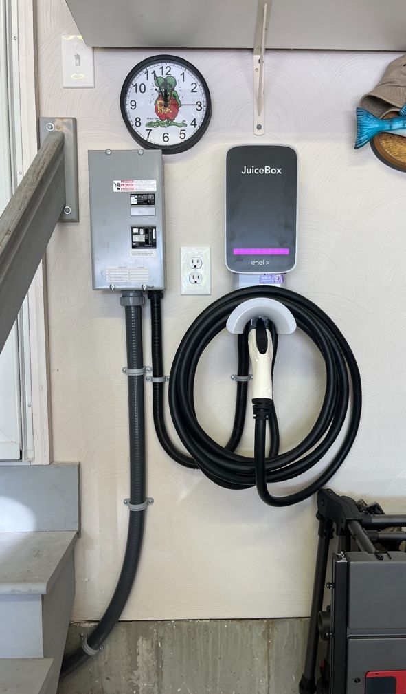 Electric vehicle charger and electrical box mounted on a garage wall, with a clock.