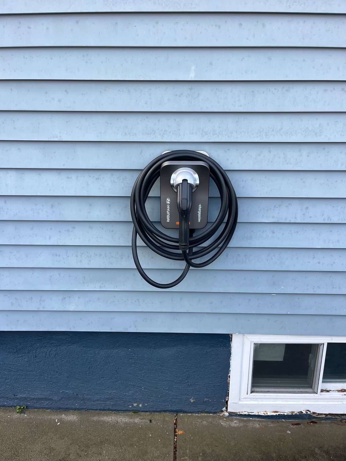 Electric vehicle charger mounted on blue siding, coiled cable.