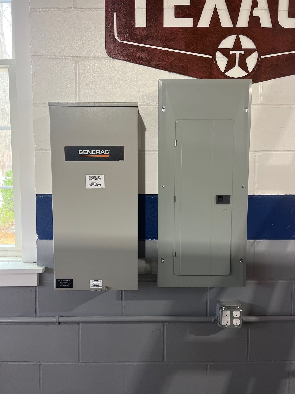 Two grey electrical panels mounted on a brick wall with a window and a Texaco sign.