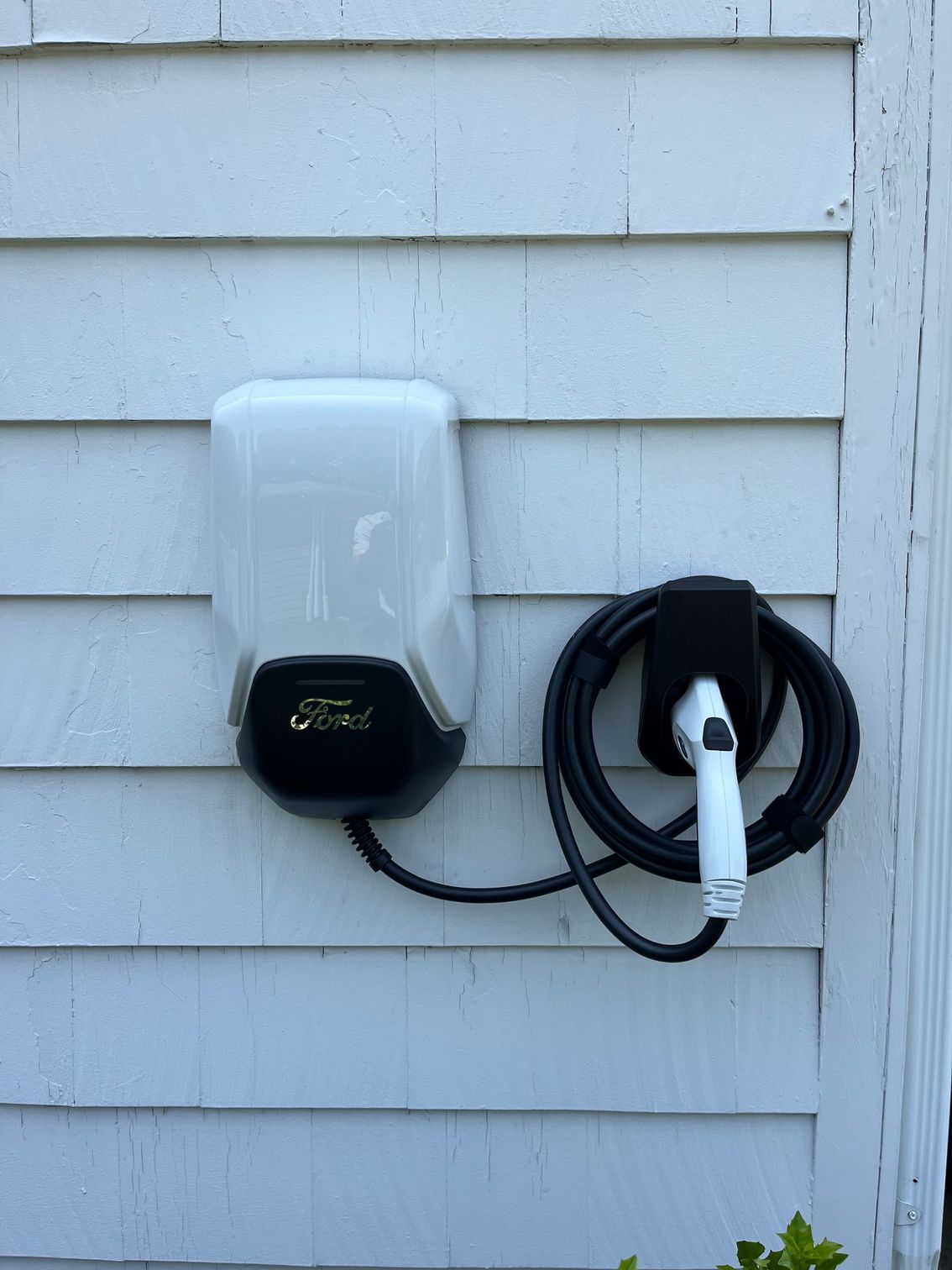 White and black electric vehicle charger mounted on a white clapboard house.