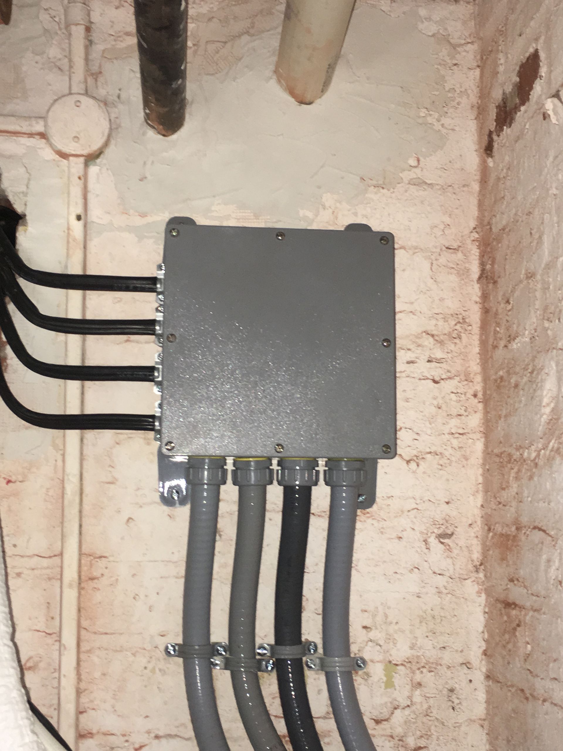 Gray electrical box mounted on a brick wall, with black and gray conduit and wires.