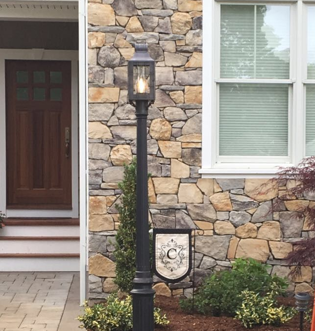 Black lamp post in front of a stone house, with a door, windows, and a ladder visible.