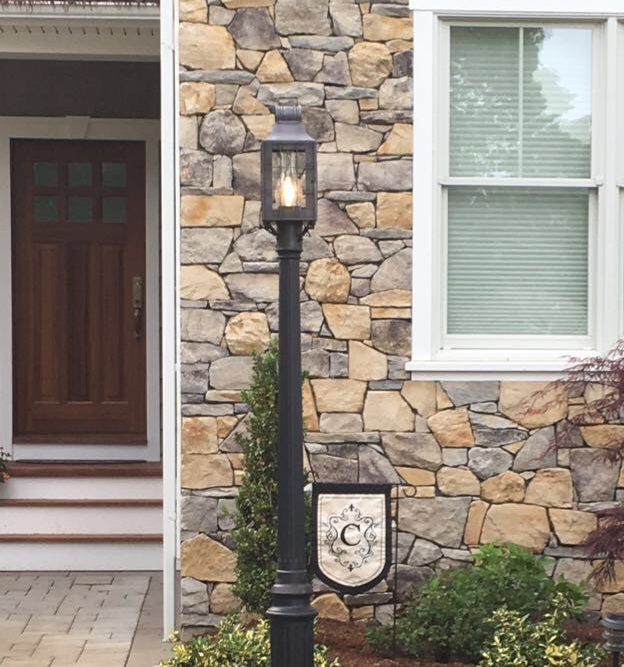 Black lamppost in front of a stone wall, next to a wooden door and white window.