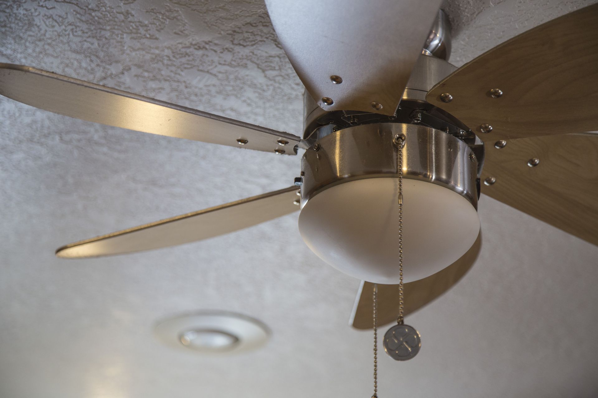 Ceiling fan with light, blades of wood and silver, mounted on textured ceiling.
