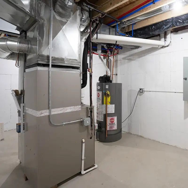 A grey furnace with metal ductwork and a tall water heater stand in a clean, unfinished basement with white walls.