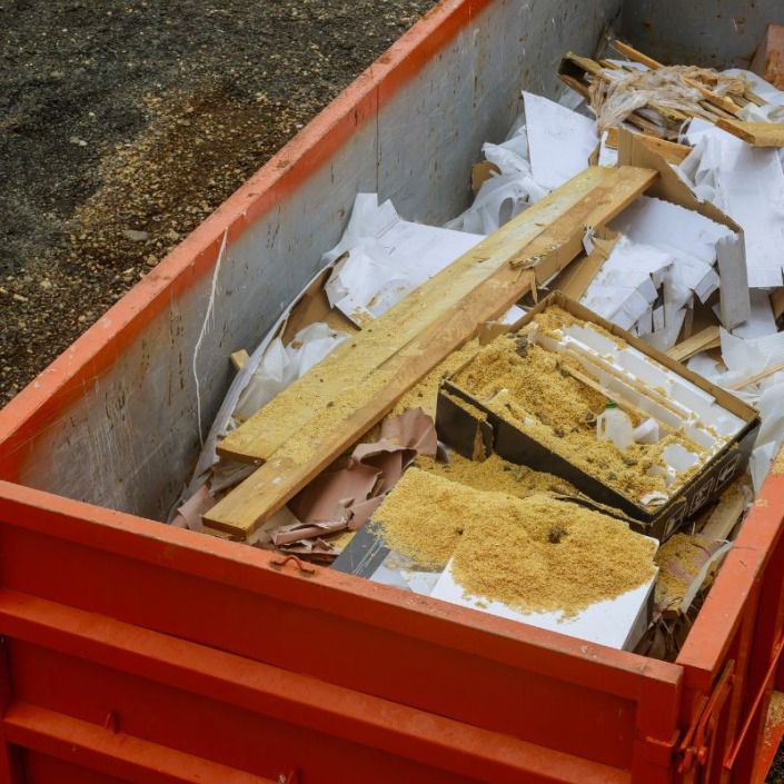 An orange dumpster filled with construction debris, including wood planks, styrofoam, and wood shavings.