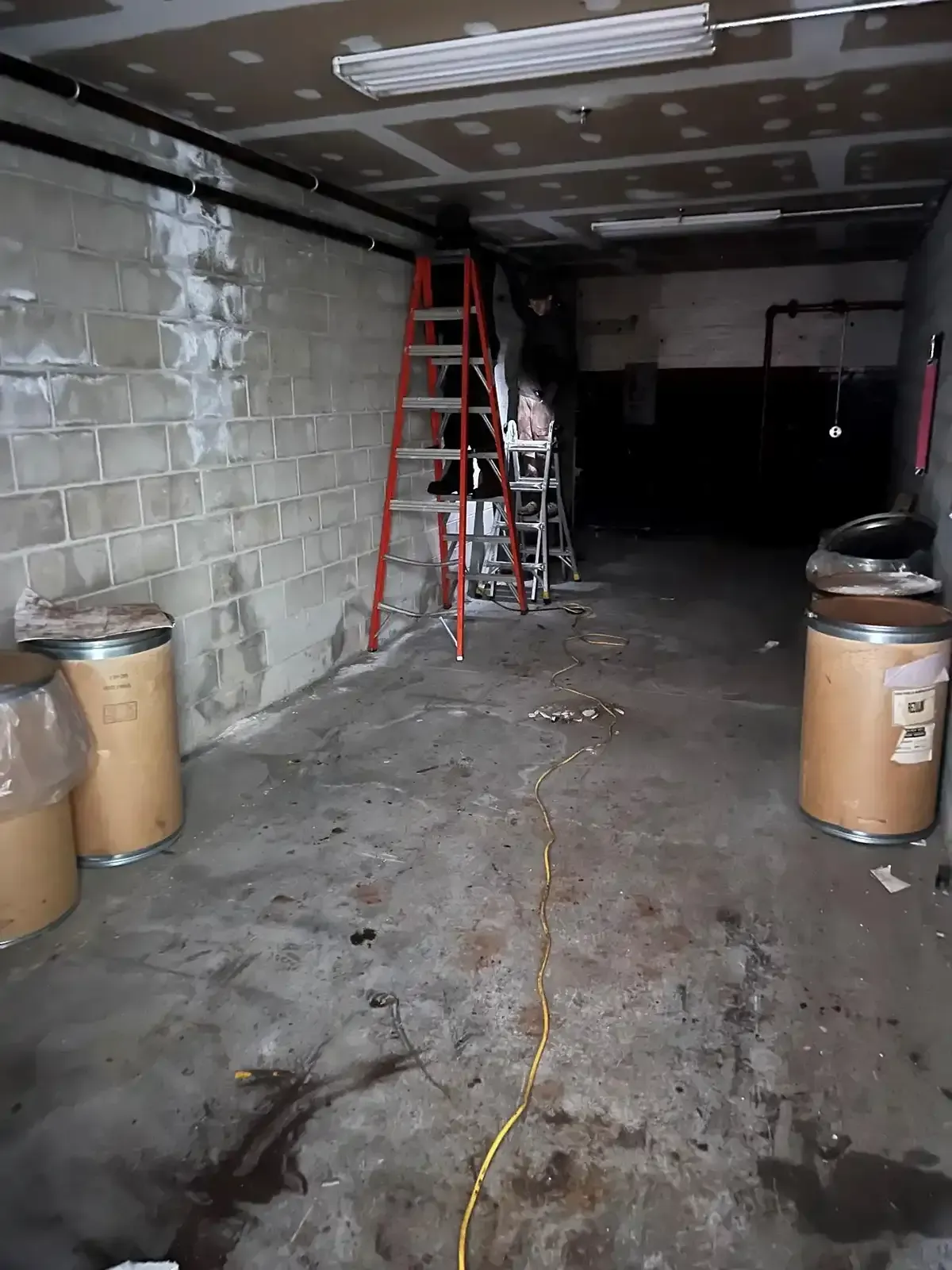 Dim empty garage with red ladder, cinder block walls, and trash bins along both sides.