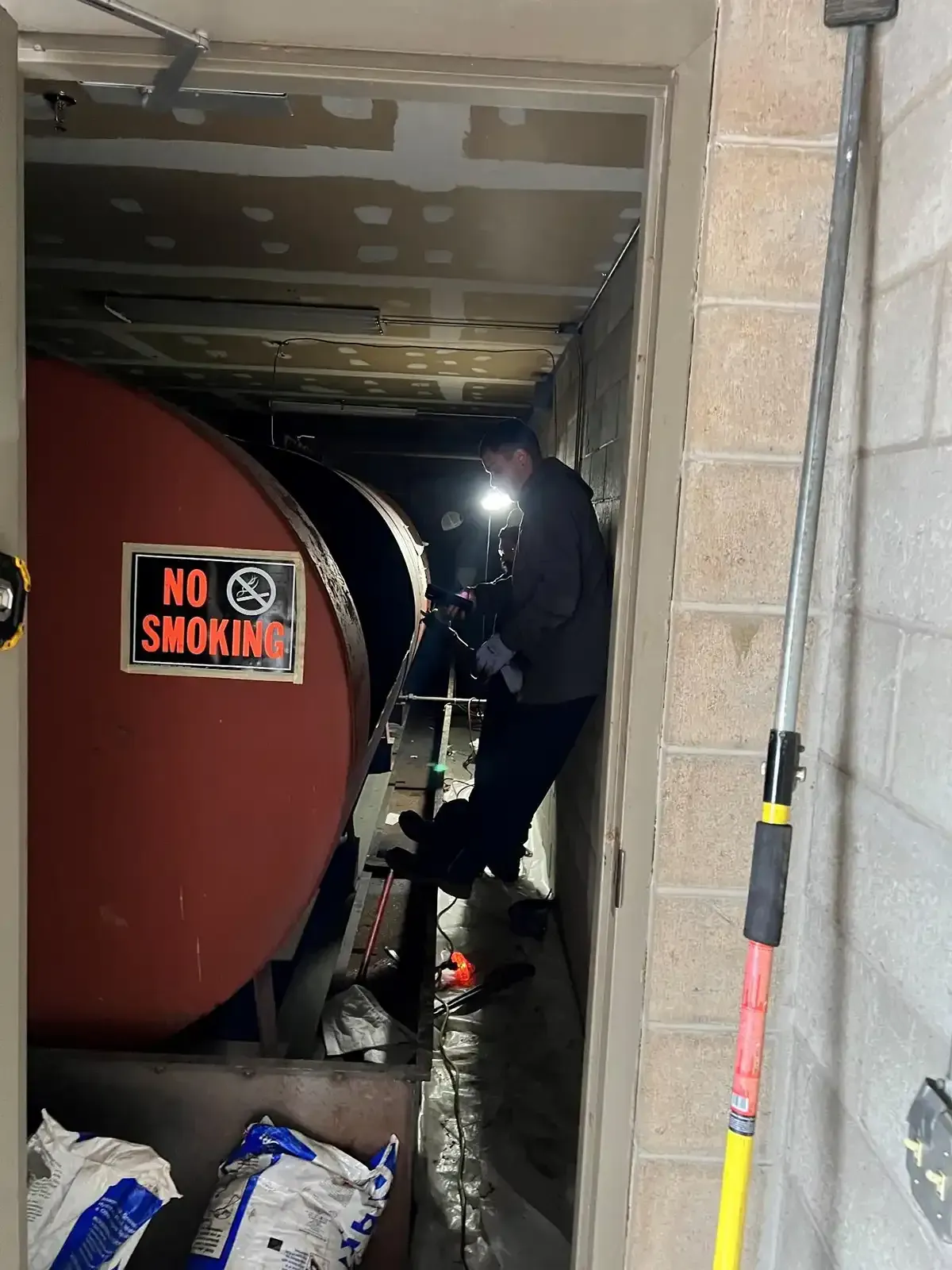 Firefighters inspecting a dark, cramped hallway beside a red “No Smoking” sign and stacked bags.