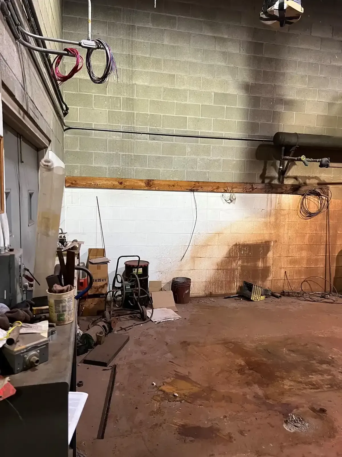 Empty industrial garage with concrete floor, cinderblock walls, and scattered tools and equipment.