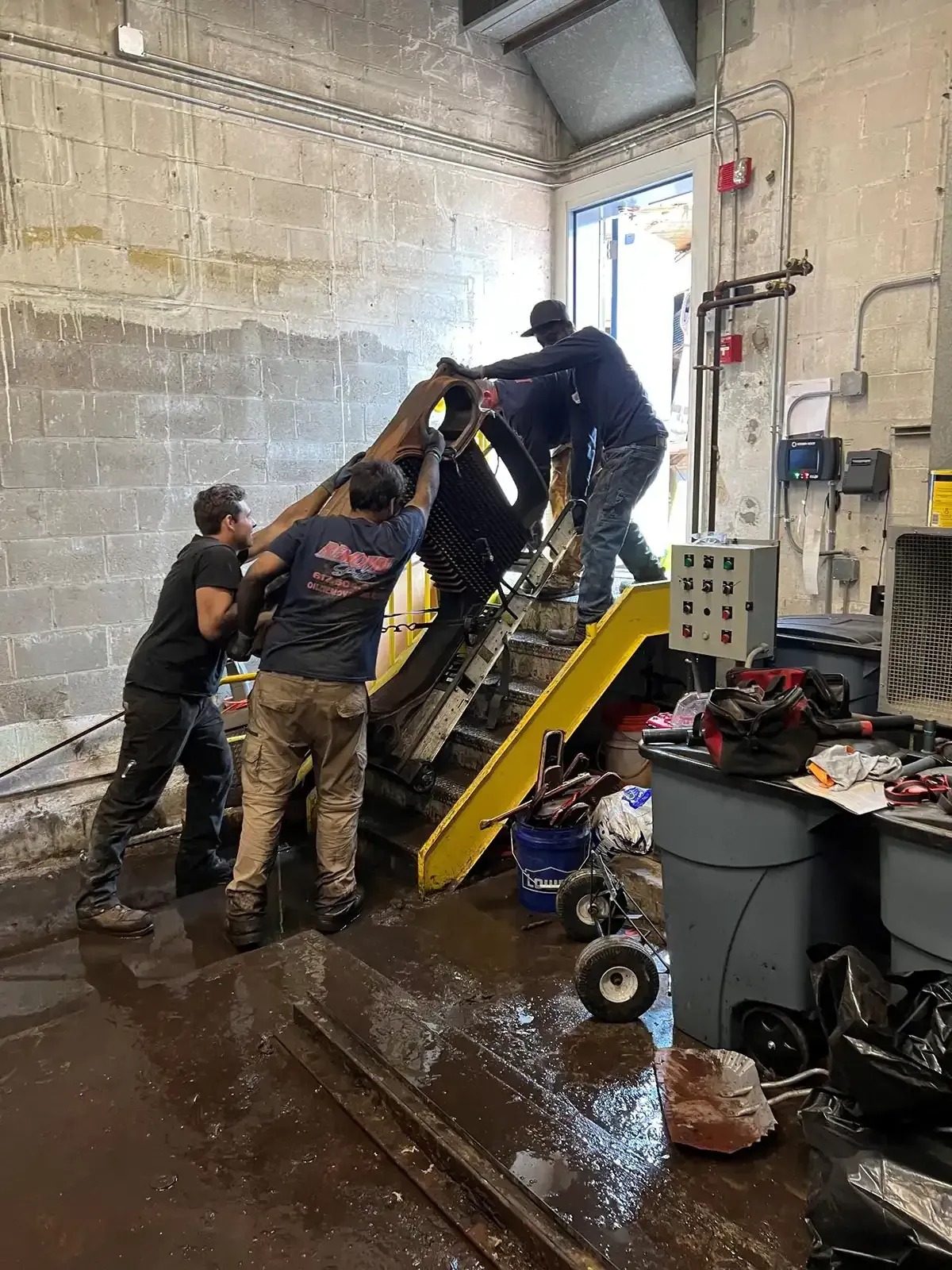 Workers pushing a large machine up a yellow ramp inside a warehouse workshop.