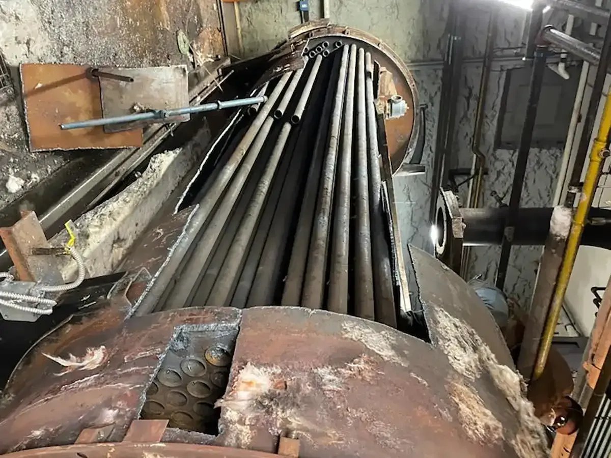 Rusty industrial pipes inside a large metal vessel or boiler, seen in a cramped machinery room.