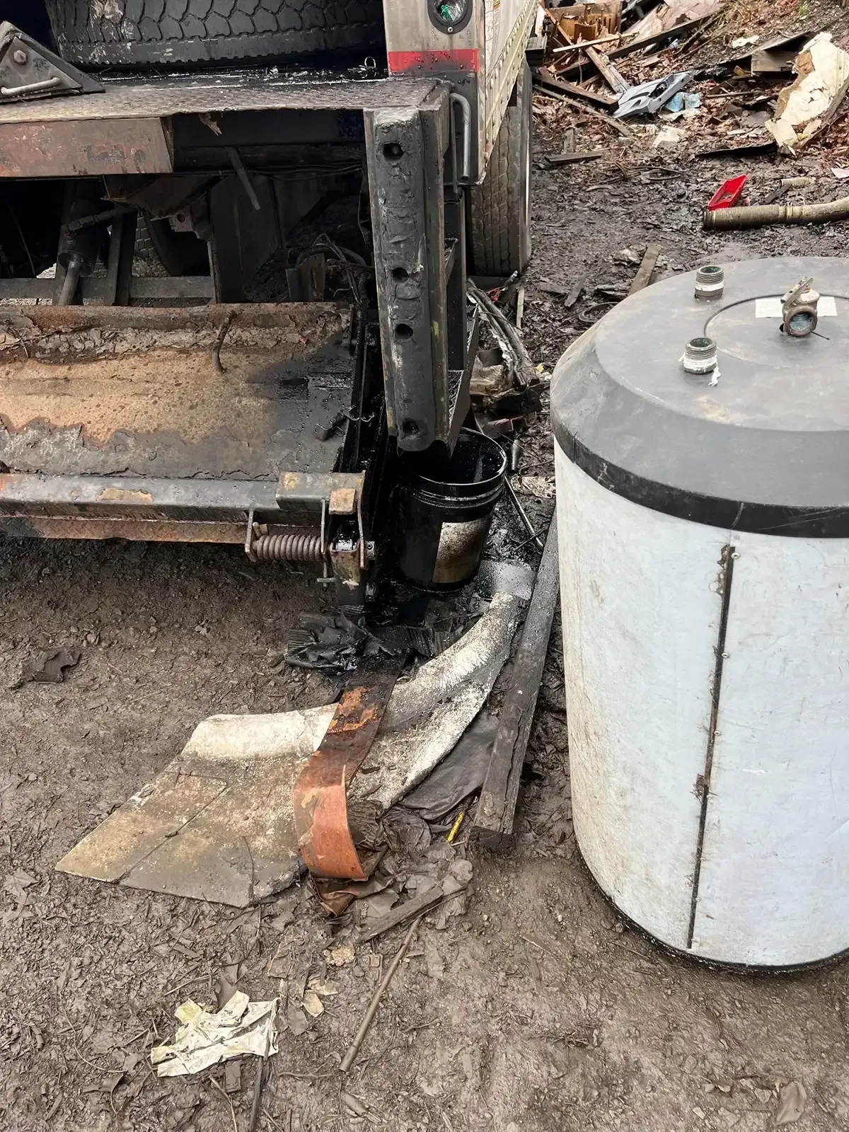 Rusty industrial machinery beside a white tank on a dirt-covered ground.