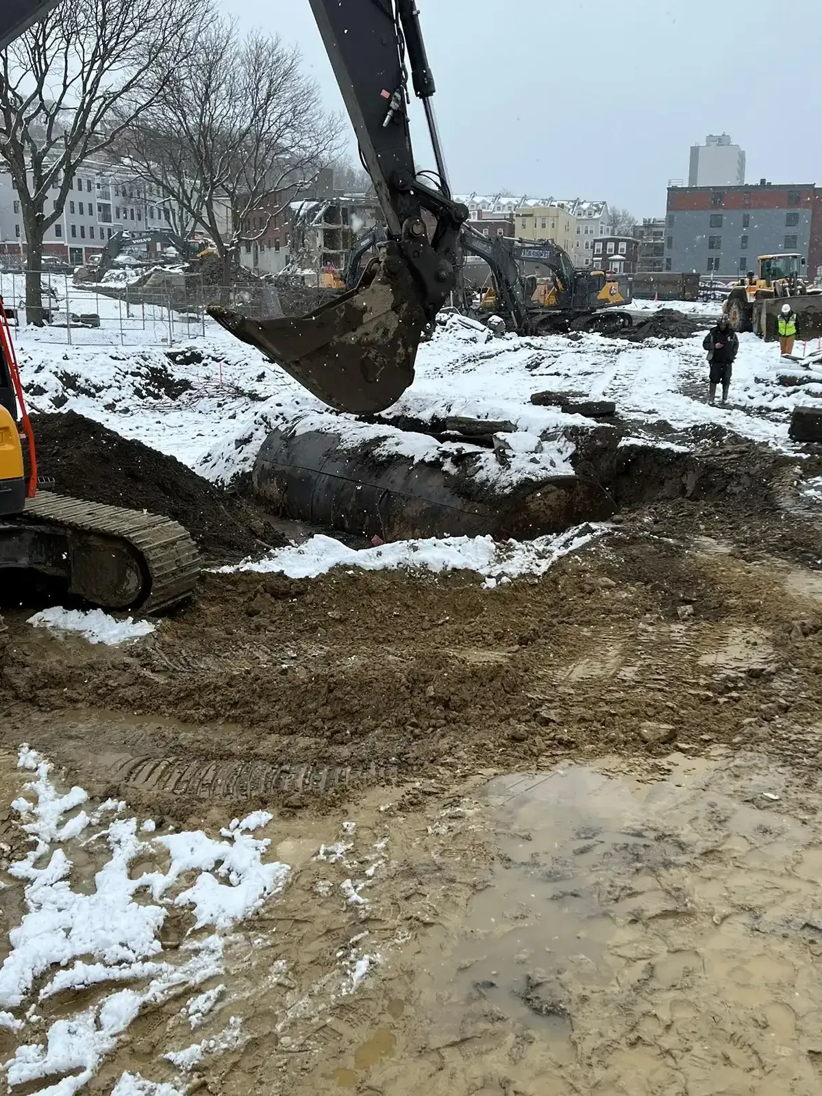 Excavator digging muddy snow-covered ground at a construction site in winter.